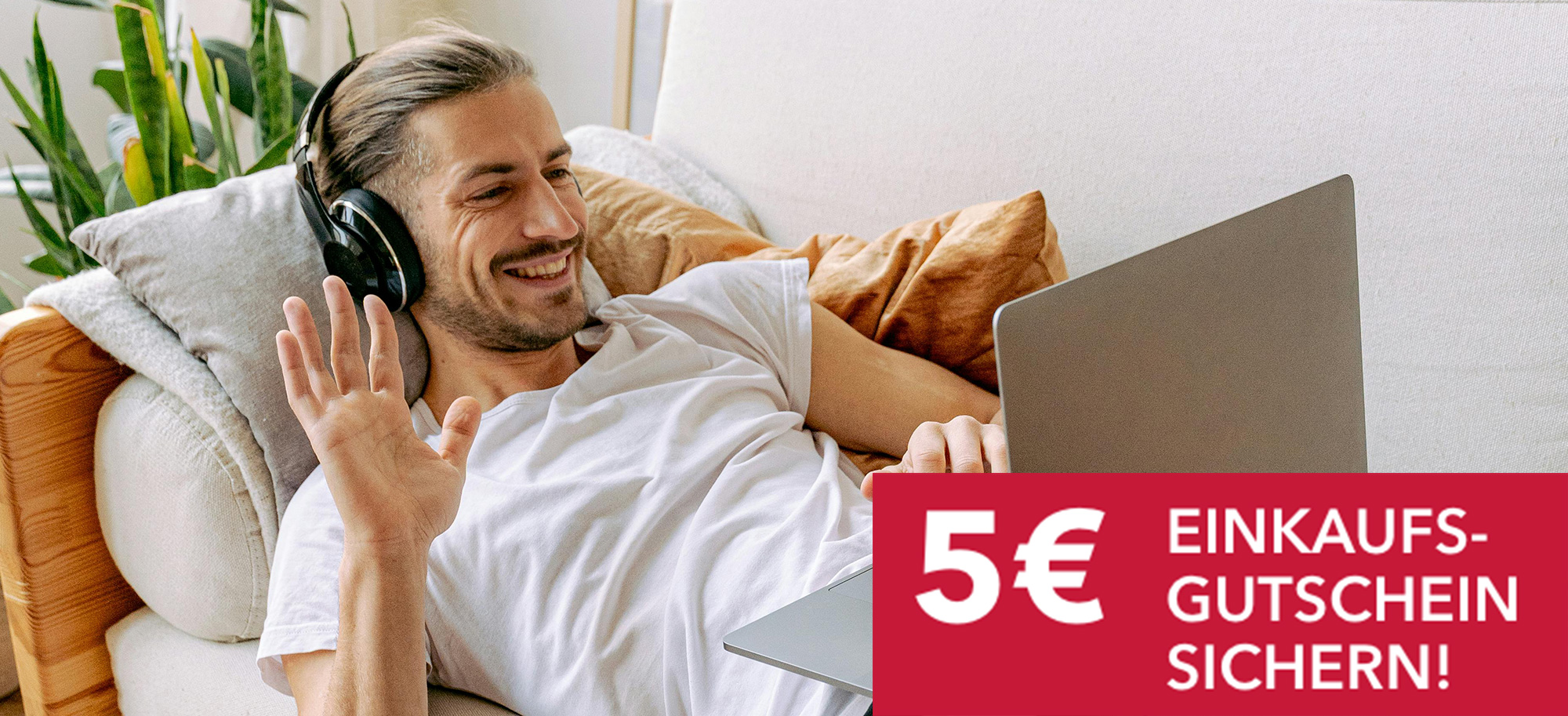 Mann mit Kopfhörern und Laptop winkt von der Couch aus, rechts unten rotes Banner mit weißem Schriftzug 5 € Einkaufsgutschein sichern!